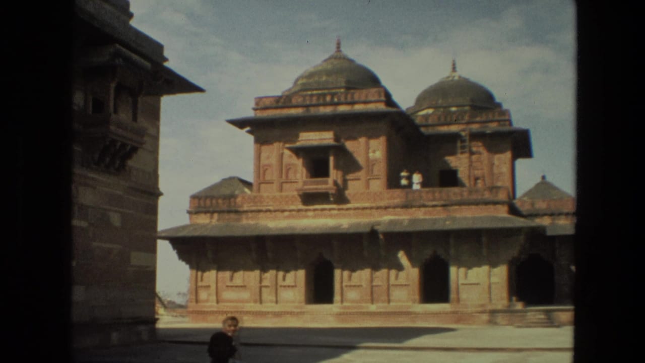 1974 India 8mm frame showing a Mughal-style red sandstone building with domes, carved walls, courtyard space, and a distant visitor.