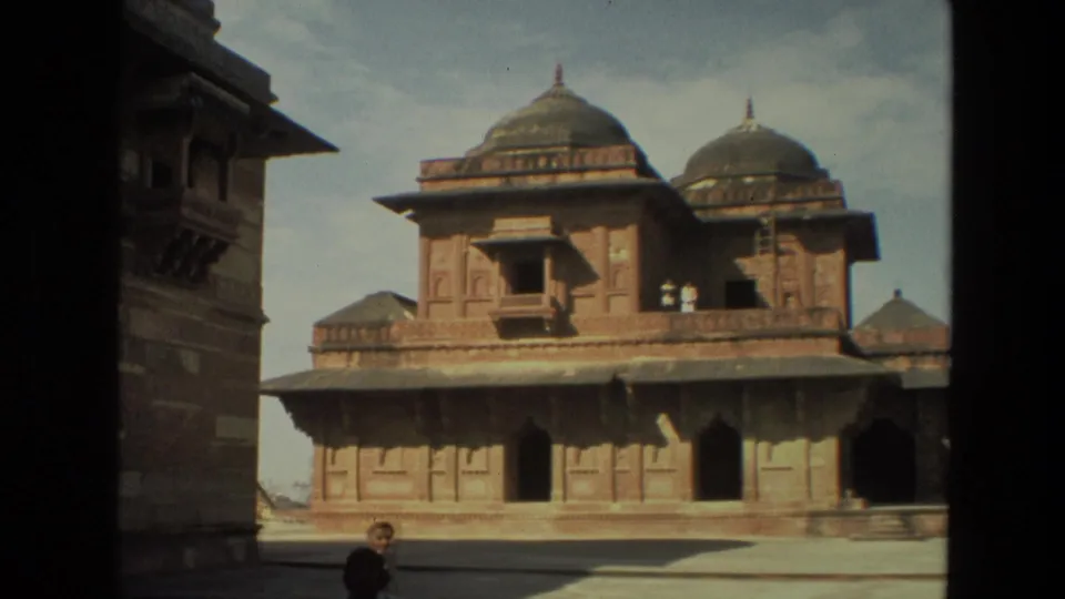 1974 India 8mm frame showing a Mughal-style red sandstone building with domes, carved walls, courtyard space, and a distant visitor.