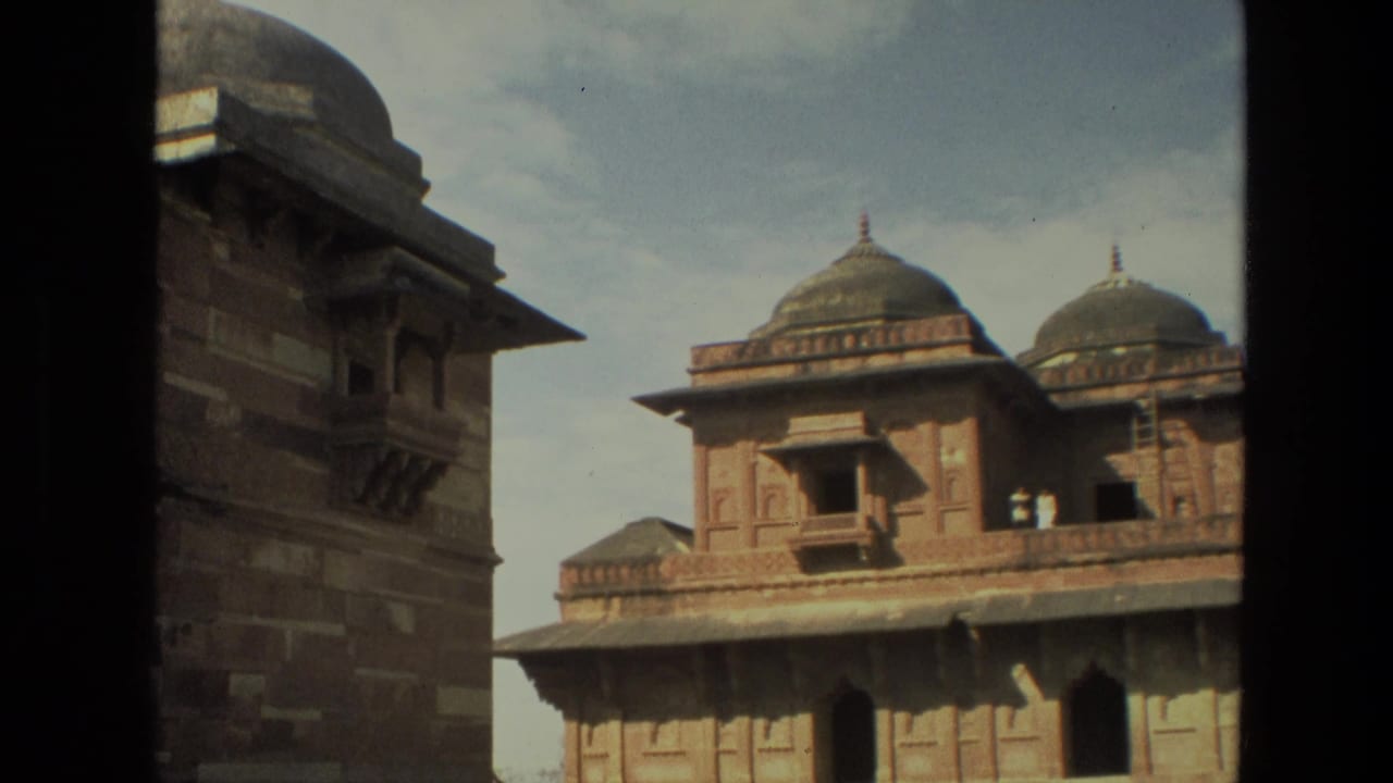 Two domed red sandstone buildings framed by a dark vertical edge under a pale blue sky.