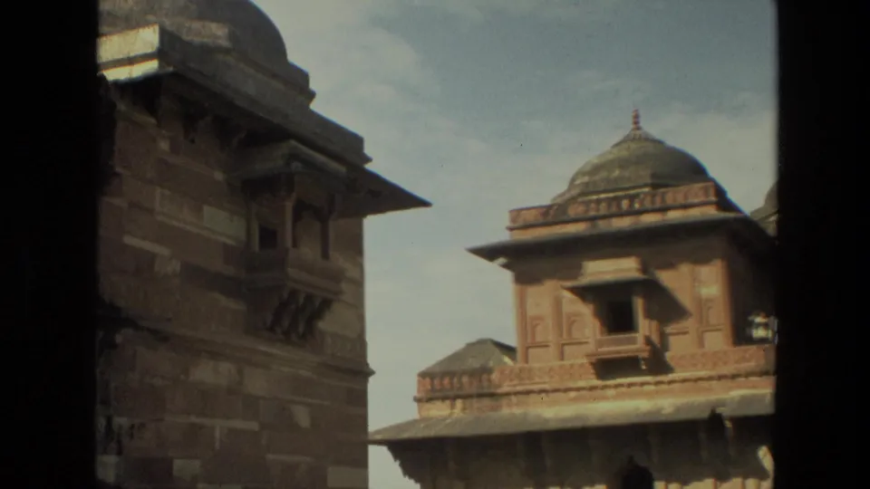 1974 India 8mm still showing a shaded architectural edge and a domed red sandstone building with carved details across a courtyard.