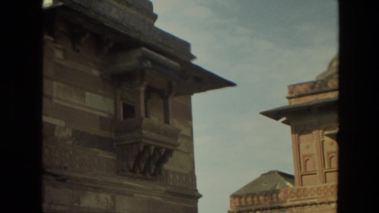 1974 India home-movie frame showing Mughal-style stone buildings viewed through a dark doorway or window frame.