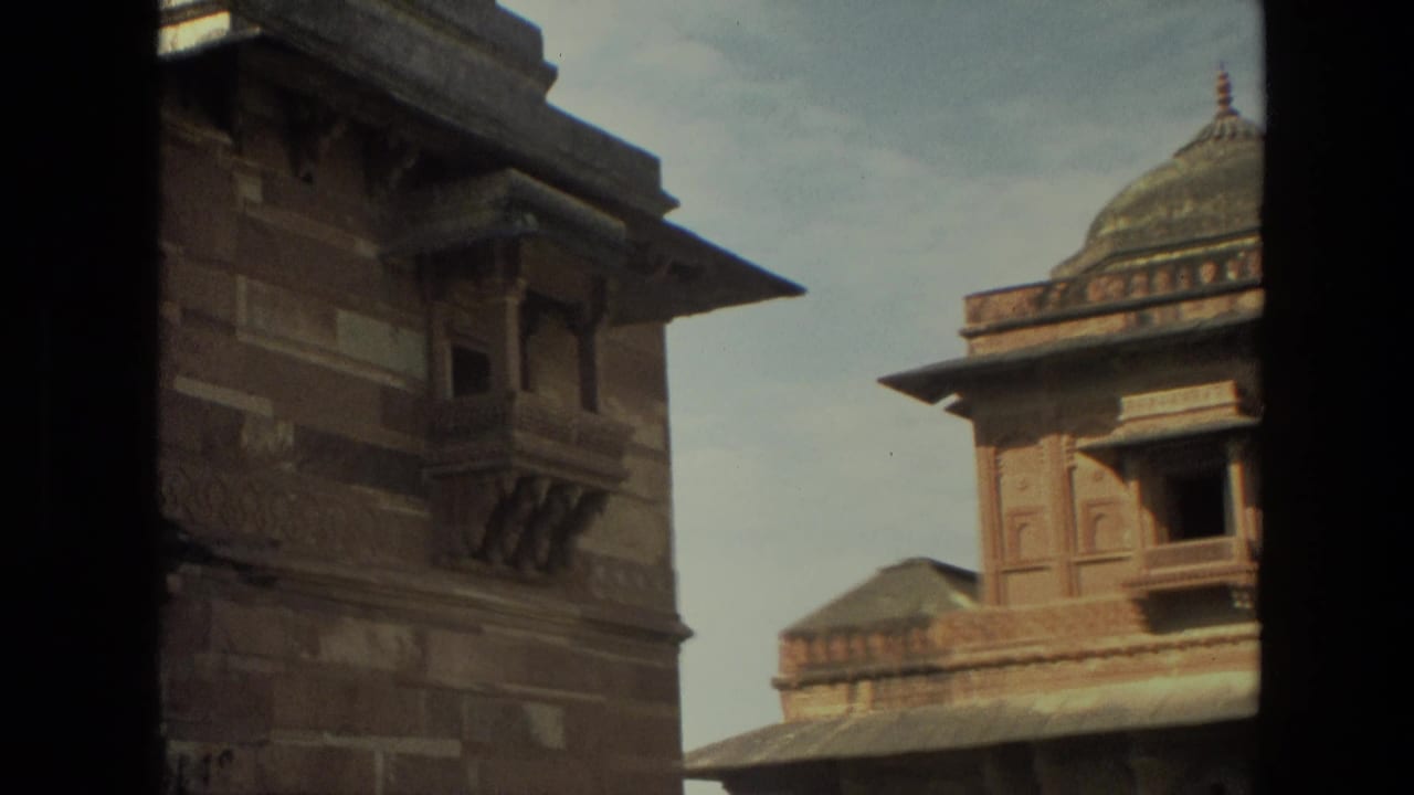 1974 India travel footage frame with a domed chhatri-like roof, carved facade, and dark foreground edge.