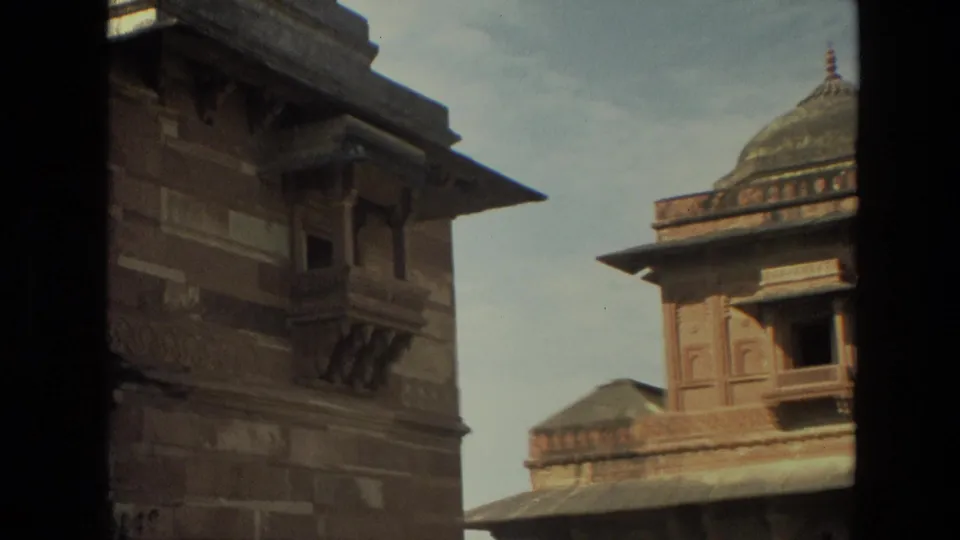 1974 India travel footage frame with a domed chhatri-like roof, carved facade, and dark foreground edge.