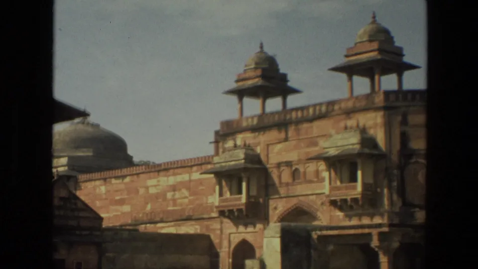 1974 India frame showing a wider view of Mughal-style sandstone architecture with chhatri-like pavilions and an arched opening.