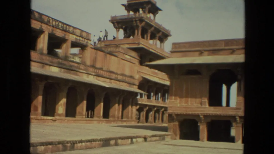 1974 8mm view in India showing a sandstone palace courtyard, arched walkways, and a raised pavilion tower under bright daylight.