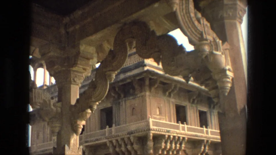 1974 India travel footage frame of carved stone arches, vertical columns, and a framed architectural view beyond.