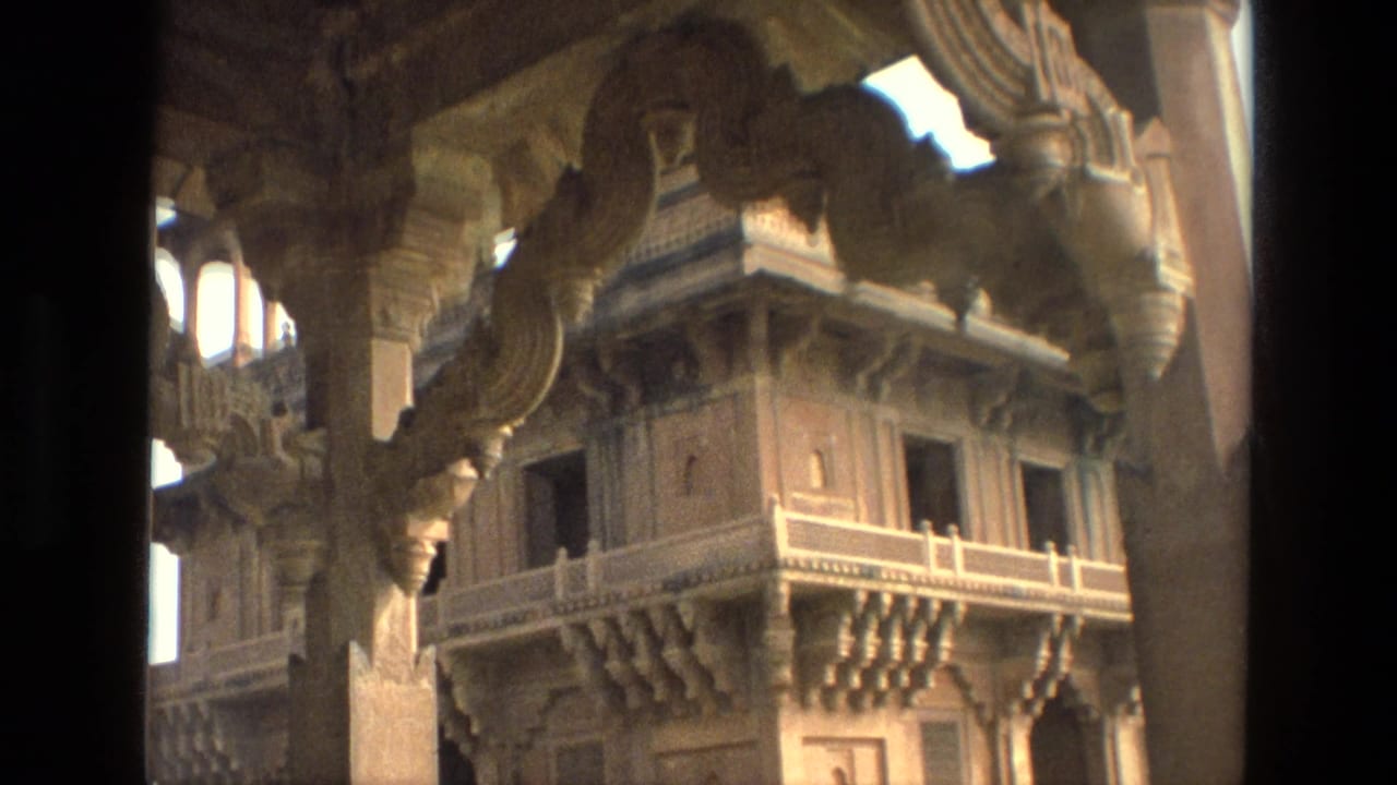 1974 India 8mm frame showing an ornate temple interior view through carved pillars toward balconies, windows, and bracketed stonework.
