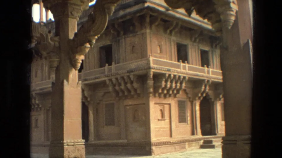 1974 India 8mm frame showing a closer visitor view of temple stonework, including pillars, balcony details, windows, and carved supports.