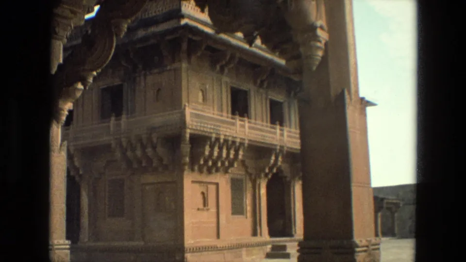 1974 India 8mm frame showing an ornate palace wall with carved balcony details and dark vertical foreground edges.
