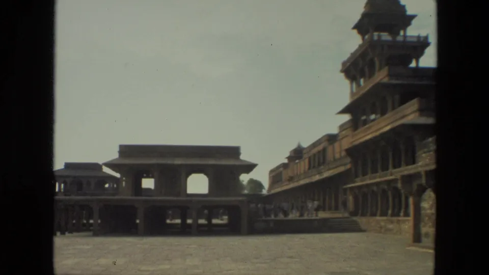 1974 India 8mm view across a palace courtyard toward arcades and a long historic facade, partially bordered by a dark foreground edge.