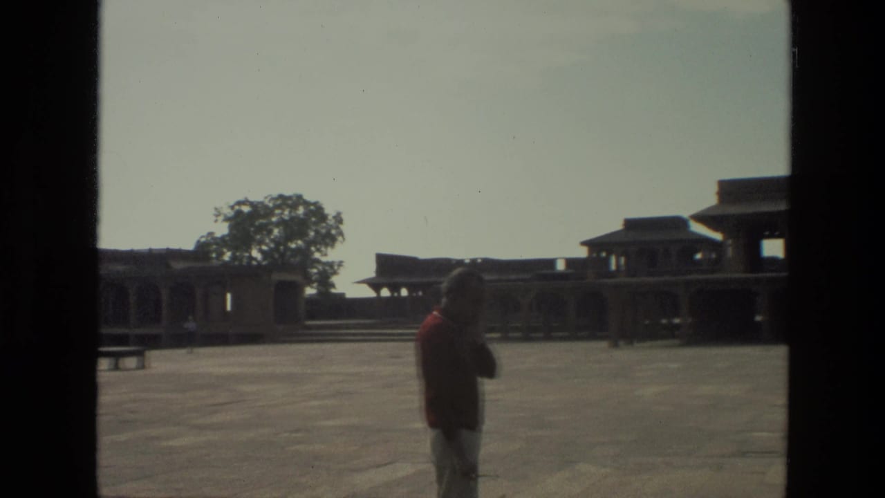 1974 India 8mm frame with a man standing in profile before open stone architecture and a mostly empty courtyard.