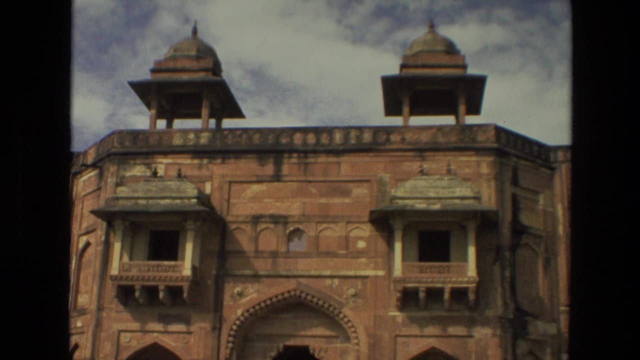 1974 India 8mm frame showing a historic red sandstone facade with arched entrances, projecting windows, and domed rooftop kiosks.