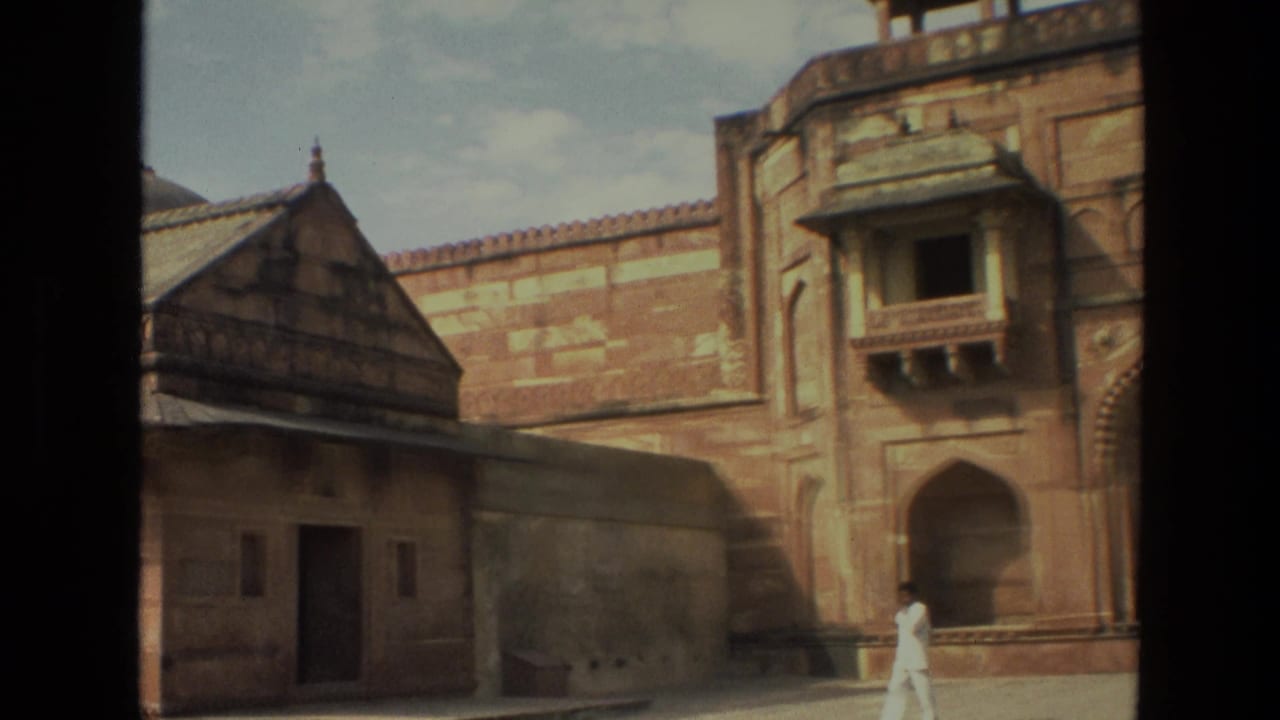1974 India 8mm frame with a palace wall, domed-roof pavilion edge, arched recess, balcony, and a man in white near the courtyard.