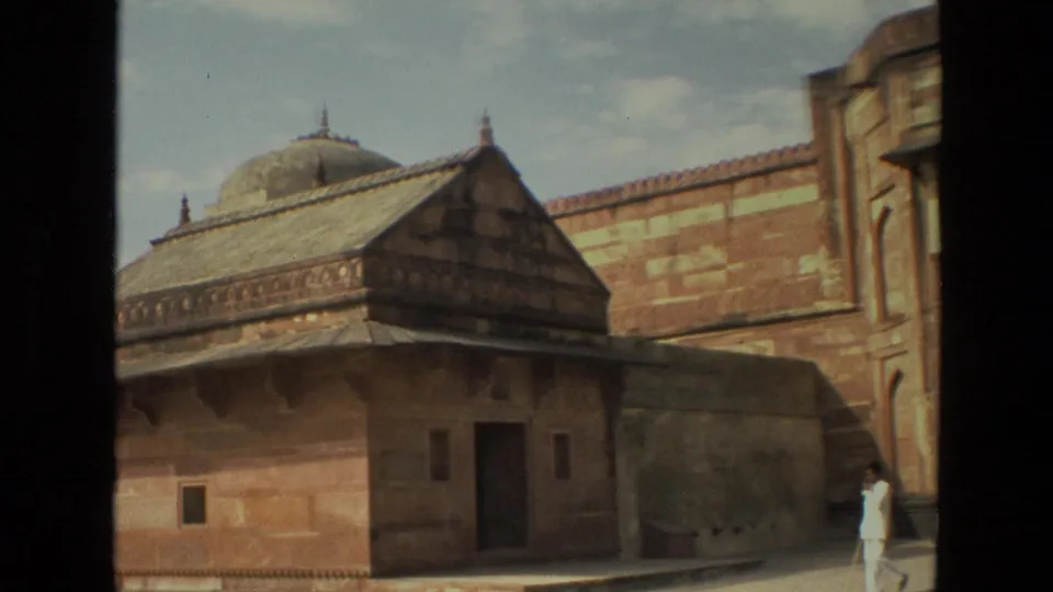 1974 India 8mm frame showing a domed pavilion, small doorway, courtyard wall, and a man in white walking through palace grounds.