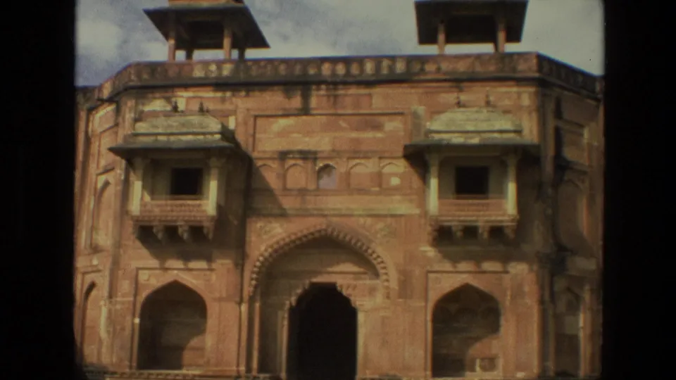 1974 India 8mm frame centered on a palace entrance with red sandstone arches, projecting balconies, dark gateway, and roofline details.
