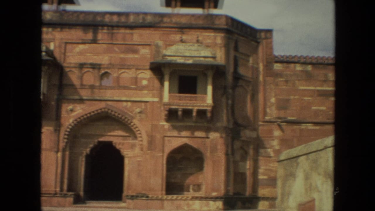 1974 India 8mm frame showing a red sandstone architectural facade with an arched entrance, projecting balcony, and soft handheld framing.