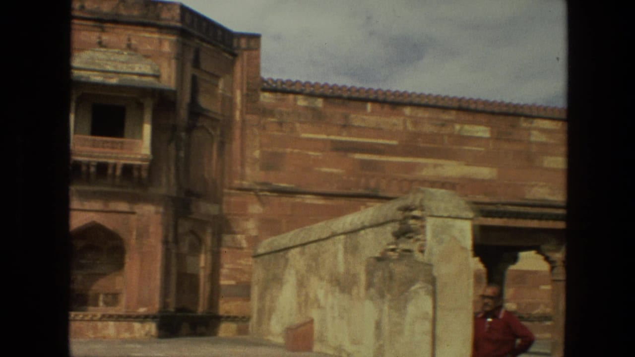 1974 India frame of a red stone courtyard wall with architectural openings and an adult man partly visible near the right edge.