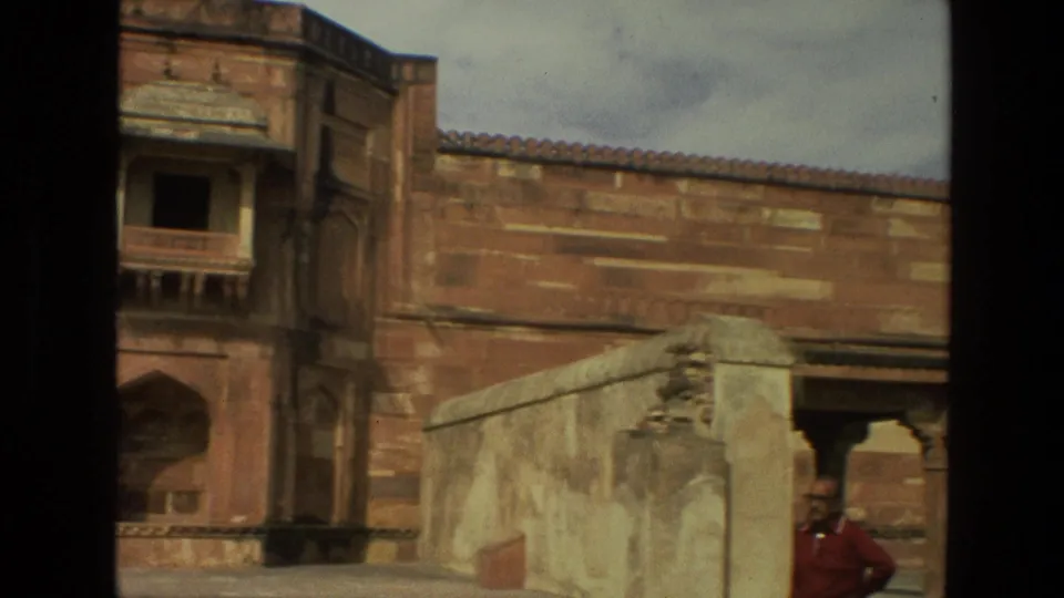 1974 India frame of a red stone courtyard wall with architectural openings and an adult man partly visible near the right edge.