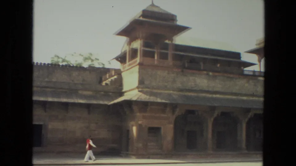 1974 India frame showing a historic courtyard building with an elevated pavilion while an adult man walks across the open foreground.