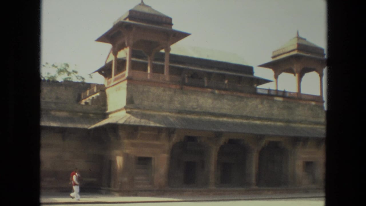 1974 India 8mm frame showing a Mughal-style sandstone facade, domed pavilion, arched colonnade, open courtyard, and a lone visitor.