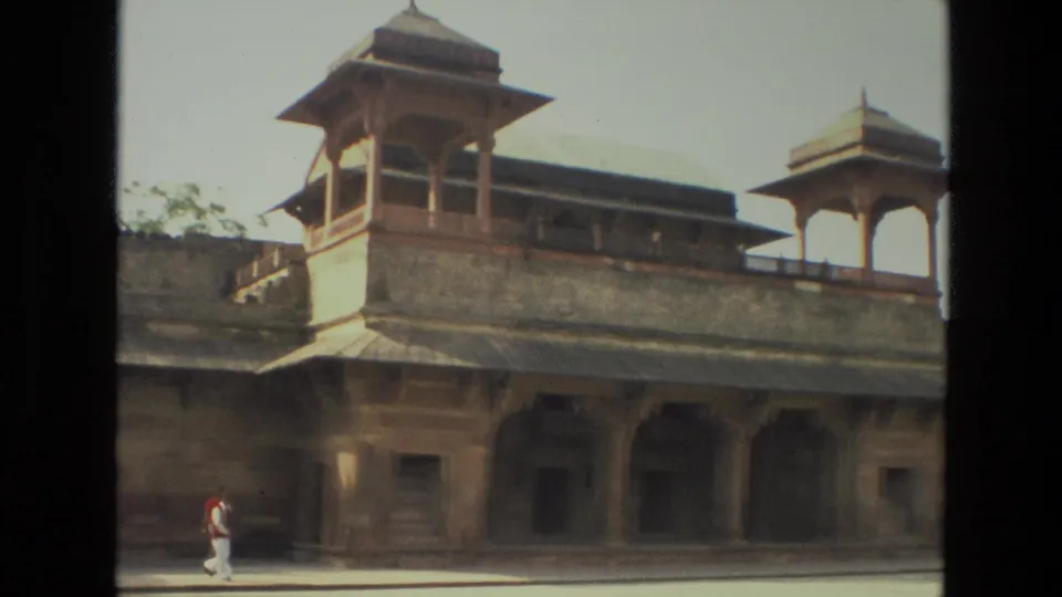 1974 India 8mm frame showing a Mughal-style sandstone facade, domed pavilion, arched colonnade, open courtyard, and a lone visitor.