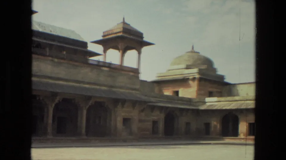1974 India 8mm frame looking across a courtyard toward arched sandstone walls, a roof pavilion, and a rounded dome behind the facade.