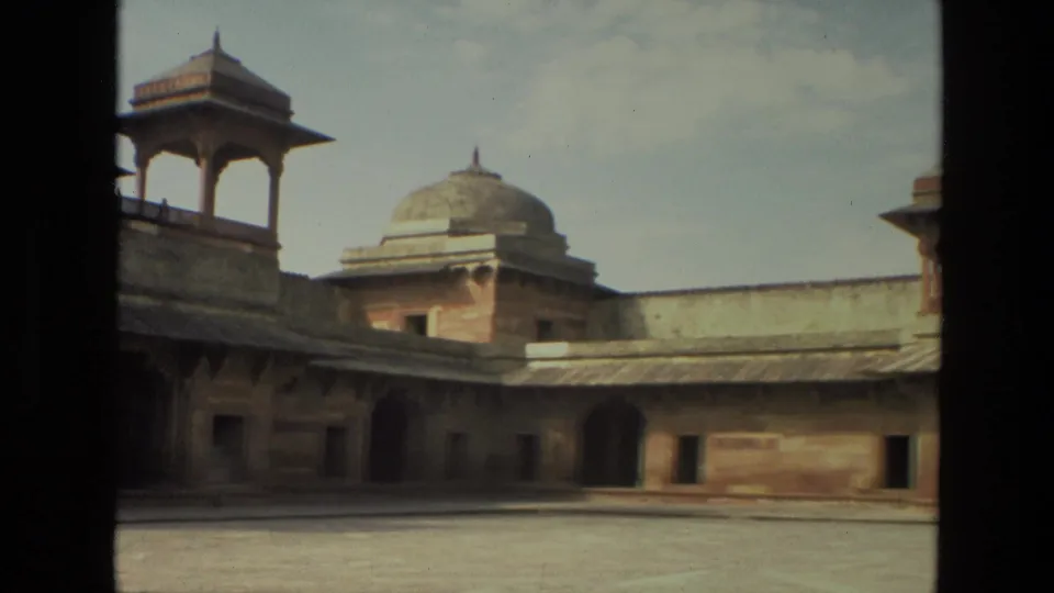 1974 India 8mm frame showing a wide courtyard view with a domed roof, elevated pavilion, arched openings, and weathered sandstone walls.