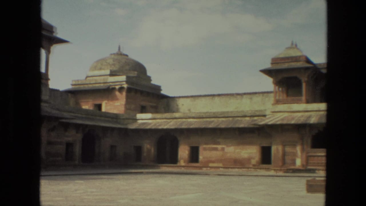 1974 India 8mm frame showing a red sandstone palace courtyard with domed pavilion roofs and arched openings, partly blocked by dark foreground edges.