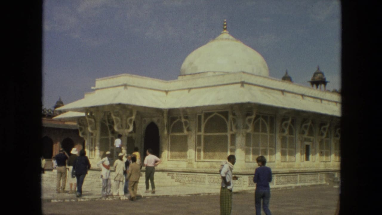 Tourists stand near a white domed mosque with arched windows under blue sky.