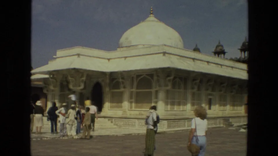 A wider 1974 India home-movie view shows tourists moving through the courtyard beside a white domed mosque.