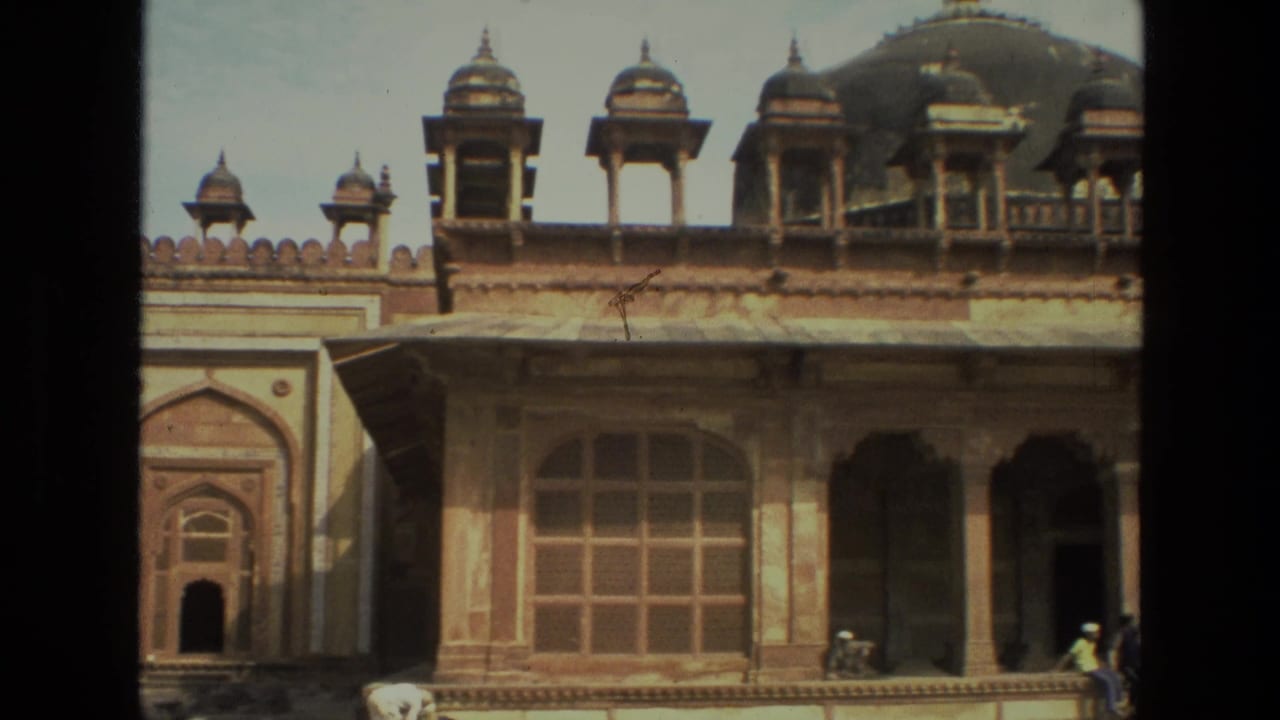 Historic sandstone facade with domes, arched windows, and visitors near the steps.