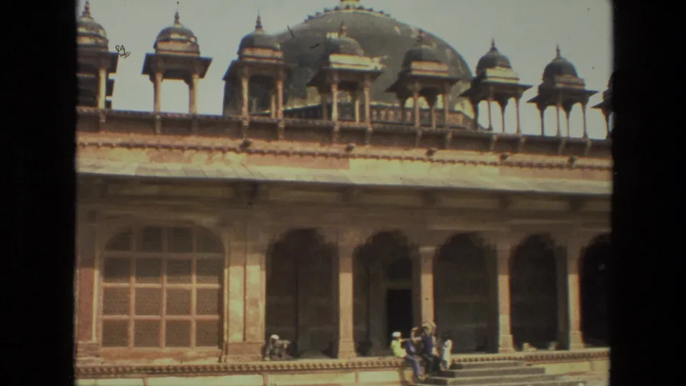 1974 India frame of a historic Mughal-era complex with chhatri-like rooftop kiosks, arched veranda bays, gridded windows, and visitors in the courtyard.