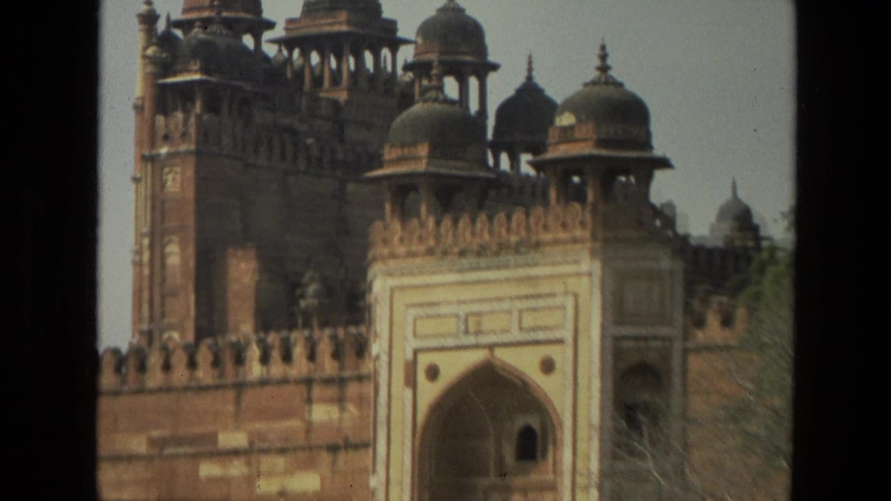 Red sandstone fort wall with domed pavilions and an arched gateway.
