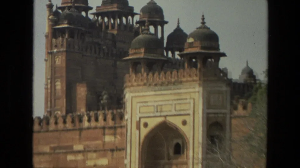 1974 India 8mm frame showing a red sandstone fort facade with crenellations, domed pavilions, and a large arched gateway.