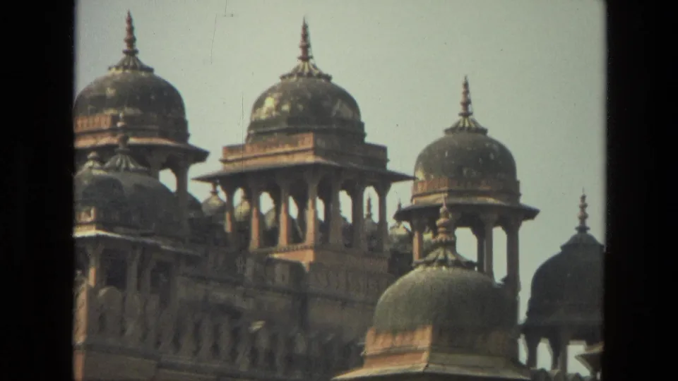 1974 India 8mm frame focused on the fort's upper domed pavilions, columns, red stonework, and pale sky.