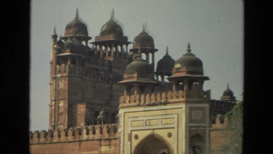 1974 India 8mm frame showing a red sandstone fort wall, arched gateway, crenellations, and several domed pavilions.