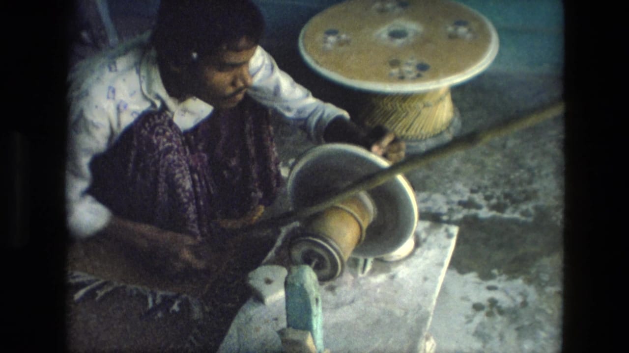 Woman seated at a low work area using a wheel-like tool beside a small round table.