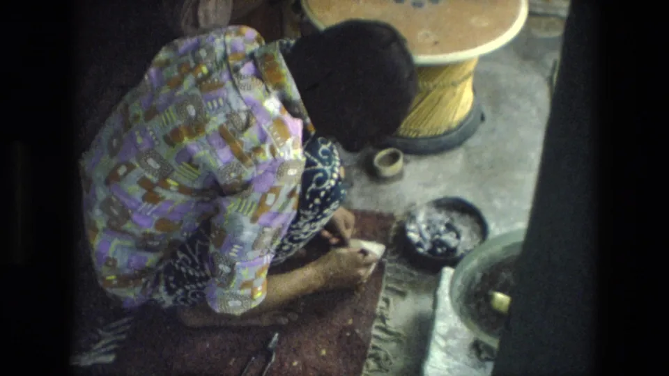 In this 1974 India frame, the woman bends over the work surface as small pieces and tools lie around her hands.