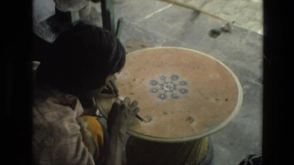 A wider 8mm frame from India in 1974 shows the woman seated beside the circular table as she works by hand.