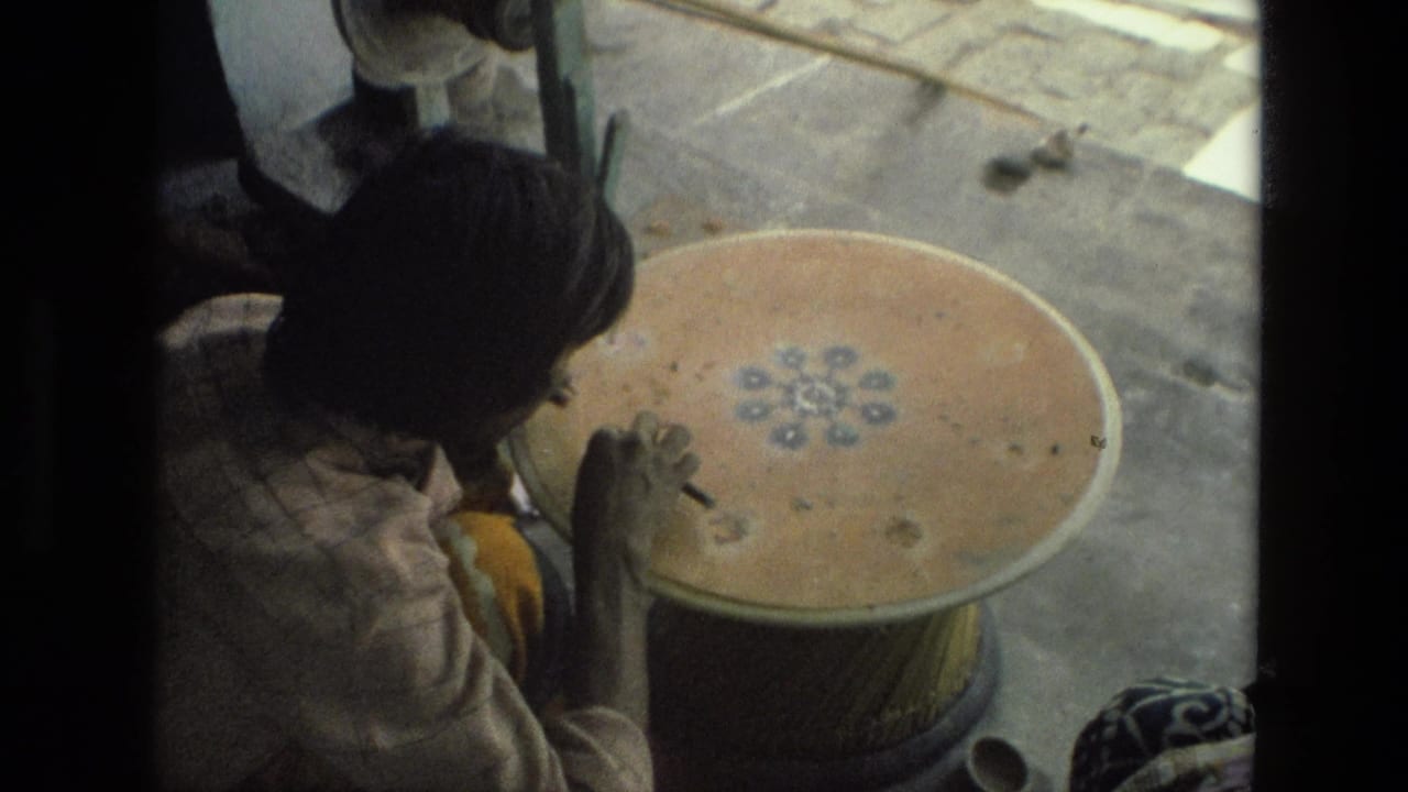Woman seated beside a large clay pot, painting a small floral design on its surface.