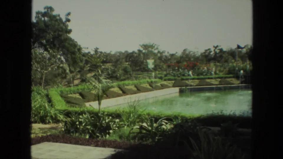 The 1974 India footage shows a formal swimming pool garden with clipped hedges, paved edging, tropical plants, and surrounding trees.