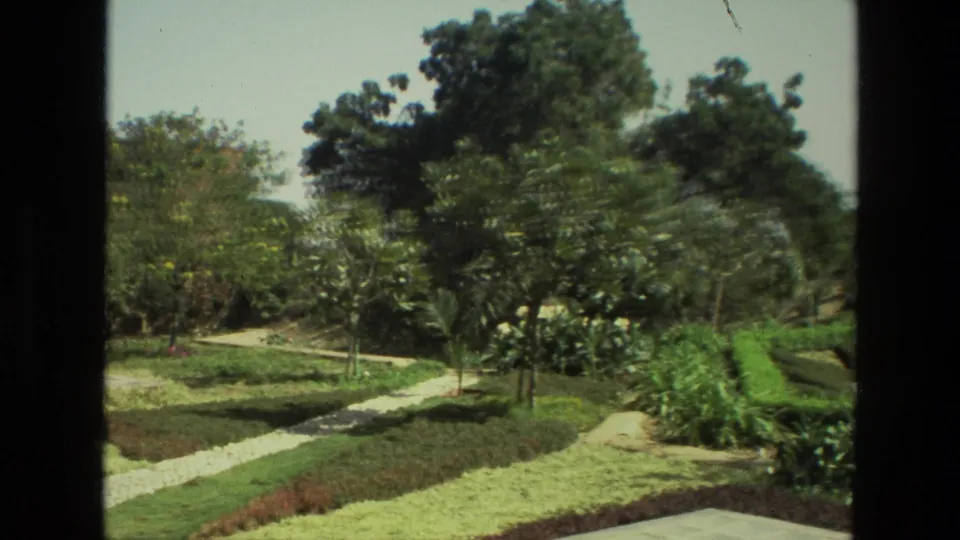 1974 India 8mm frame with slight motion blur across trees, low hedges, grass, and a winding stone path.