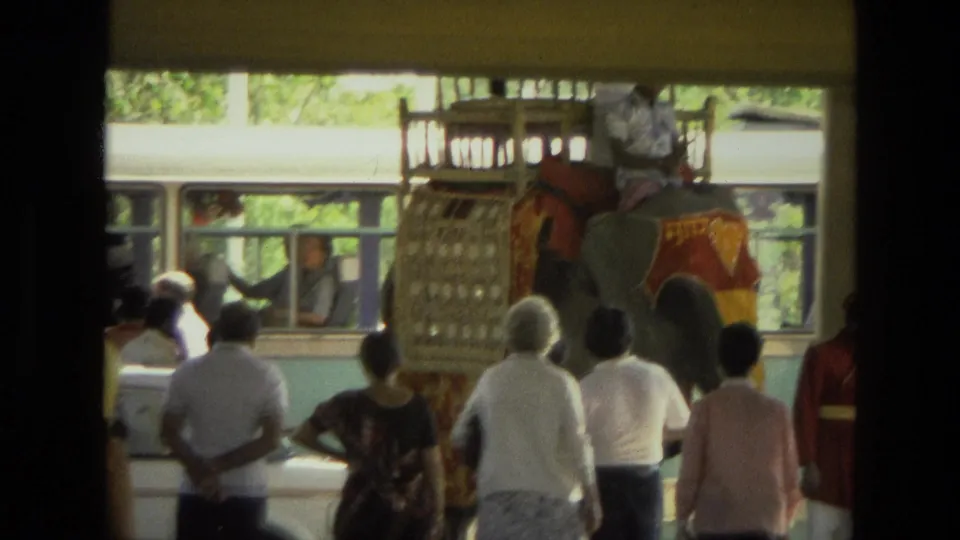 1974 India 8mm frame showing a decorated elephant carrying a rider or handler near onlookers, with a bus behind the crowd.