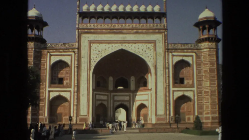 A large Mughal-style gateway appears with visitors gathered near its arched entrance in India travel footage.