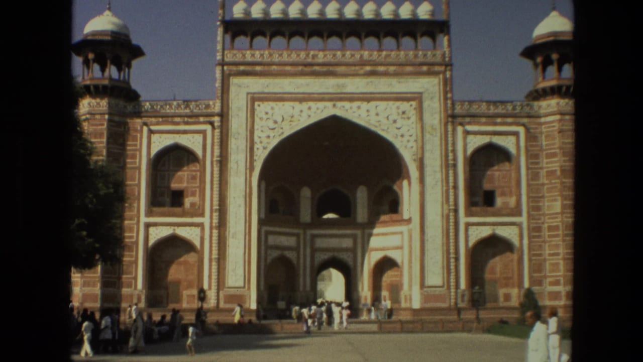 Tourists walk near an ornate arched gateway with red and white stonework.
