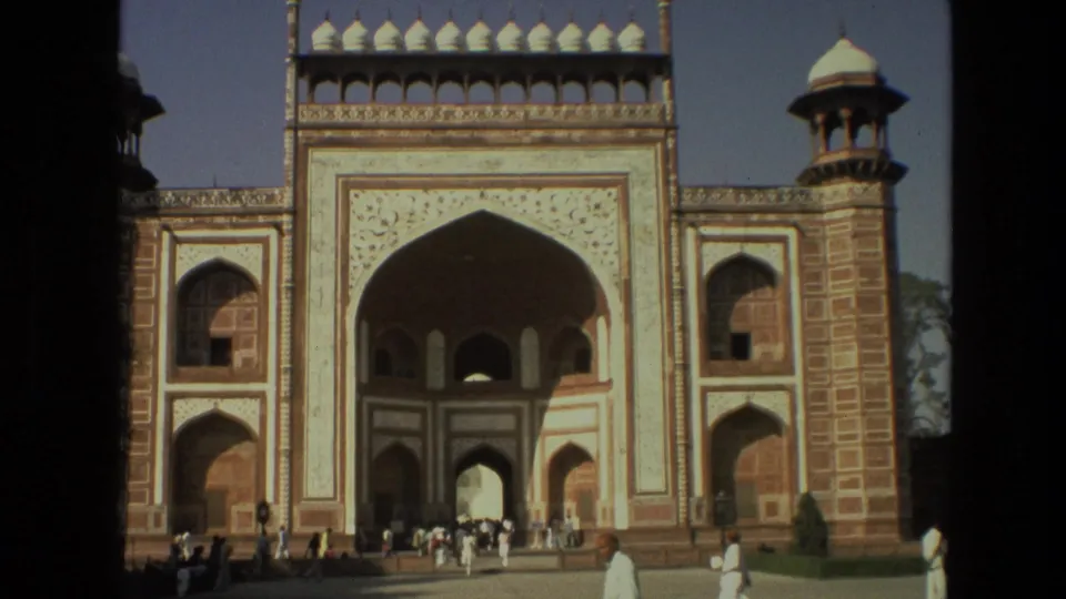 Visitors stand and walk before the monumental arched gateway at the Indian site identified in metadata as the Taj Mahal entrance.