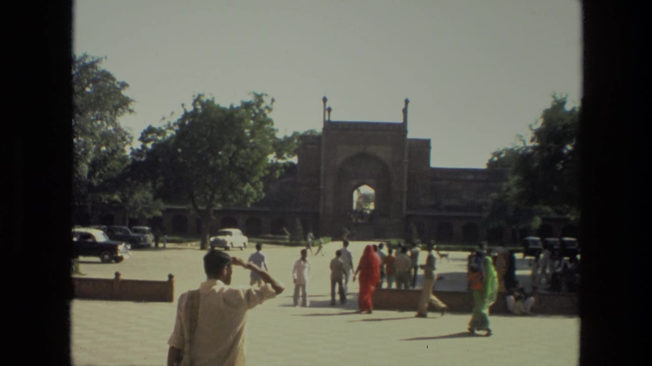 A man shades his eyes as visitors gather near the arched gateway.