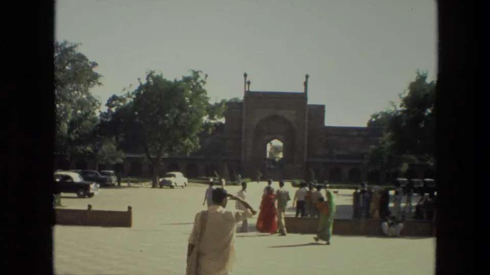 1974 home-movie view of visitors walking through the Taj Mahal complex courtyard near an arched gateway.