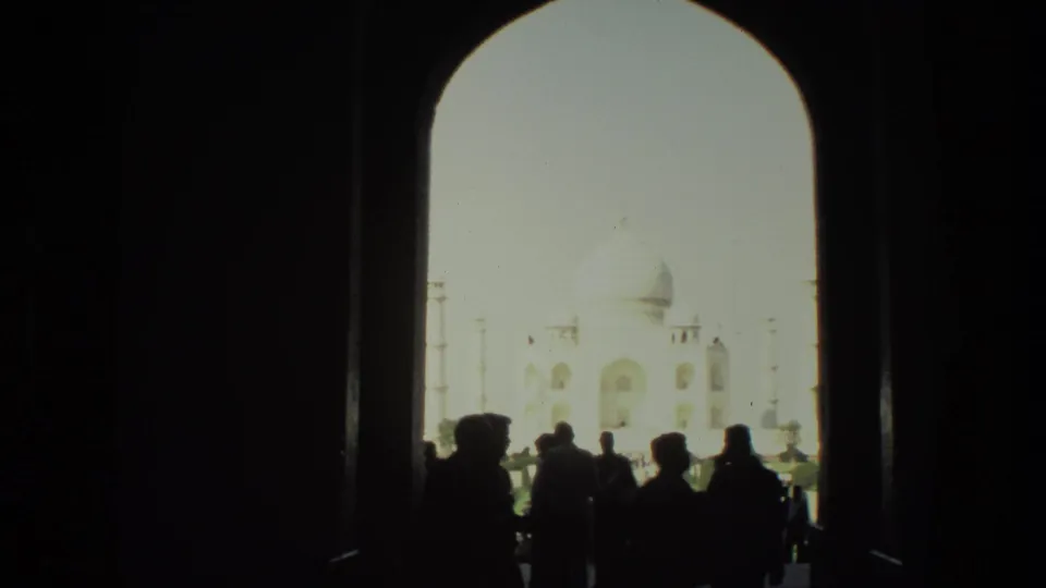 The Taj Mahal is framed through a shaded arch, with silhouetted visitors standing in the foreground.