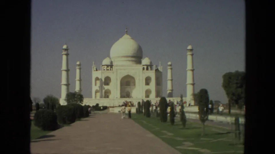 1974 8mm travel frame of the Taj Mahal from the garden approach, with tourists moving near the path and shrubs.